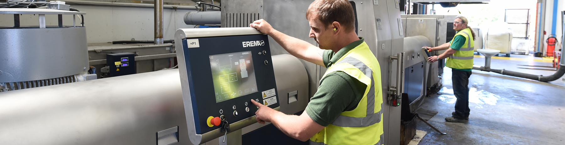 A man wearing a high-visibility jacket stands at the controls of a plastic recycling machine