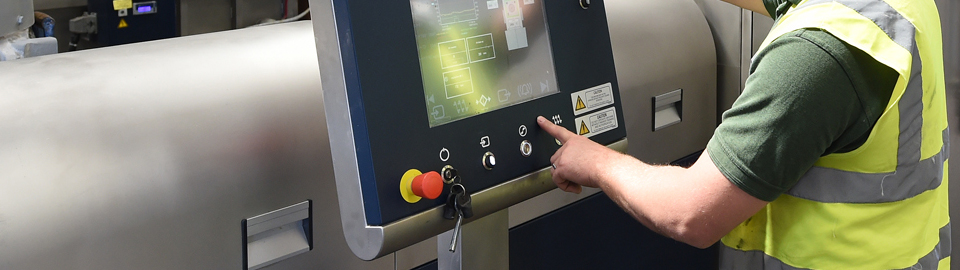 A man wearing a high-visibility jacket operates plastic recycling machinery.