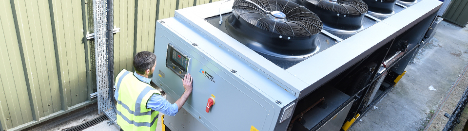 A man wearing a high-visiblity jacket stands at the controls of a plastic recycling machine.