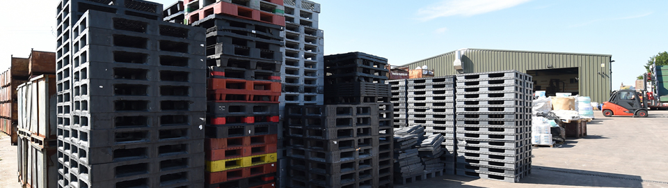 Stacks of plastic pallets outside a green warehouse.